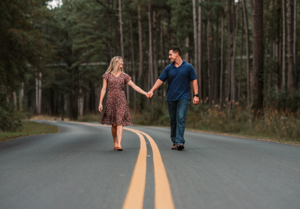 a couple walks down the middle of the street holding hands while taking congaree national park engagement photos