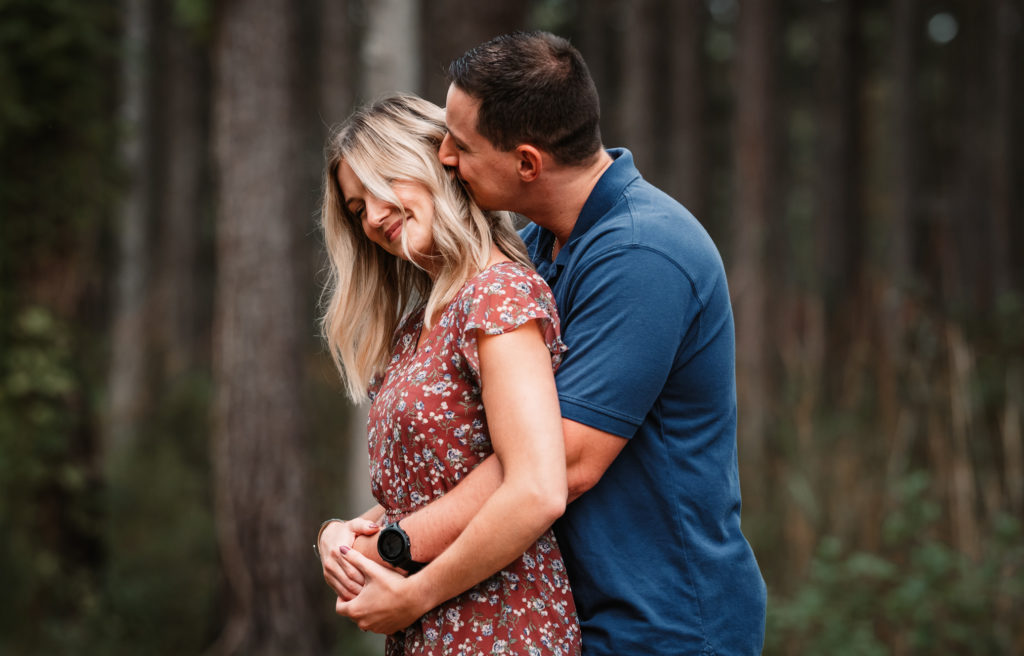 a man kisses his fiance on the side of her head and she smiles while taking congaree national park engagement photos
