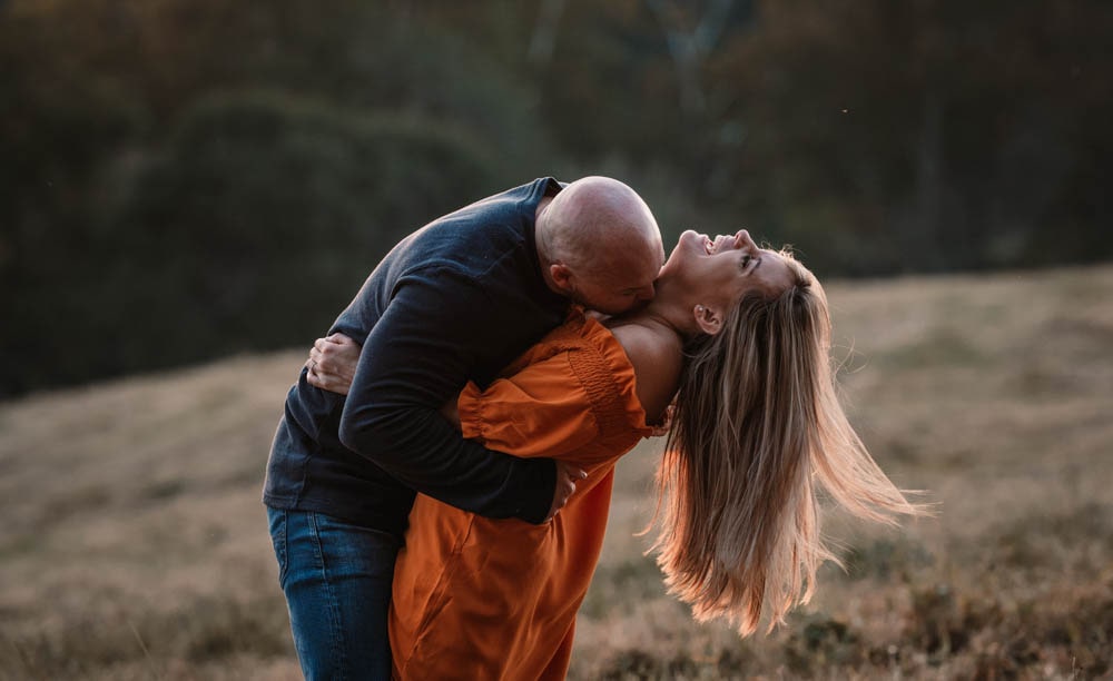 a woman is laughing while her fiance hugs her during engagement photos