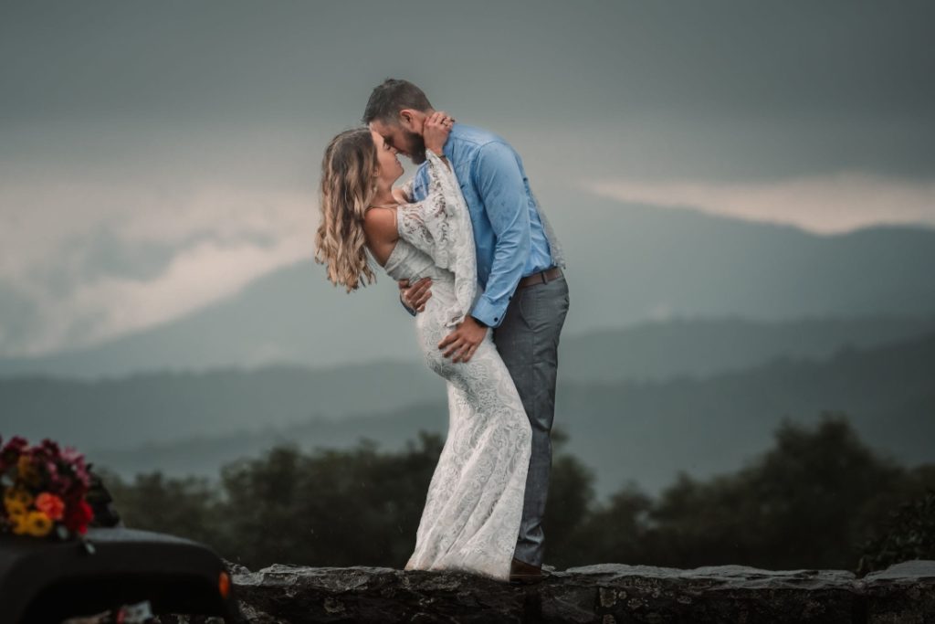 a man dips a woman backward as they kiss on a mountain after eloping