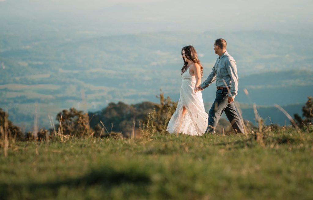 a man and woman holding hands while walking across a mountain view in the best places to elope in north carolina